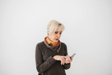 Modern bir pozitif yaşlı kadın cep telefonu tutuyor ve onu kullanıyor. Eski nesil ve modern teknoloji.