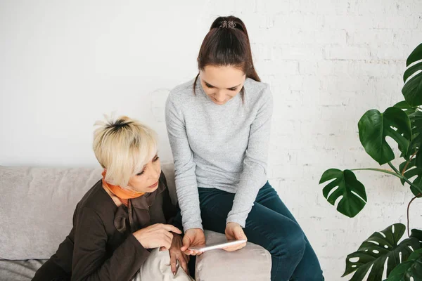 Una joven le explica a una anciana cómo usar una tableta o muestra alguna aplicación o le enseña cómo usar una red social. Enseñar a la generación más antigua de nuevas tecnologías . — Foto de Stock