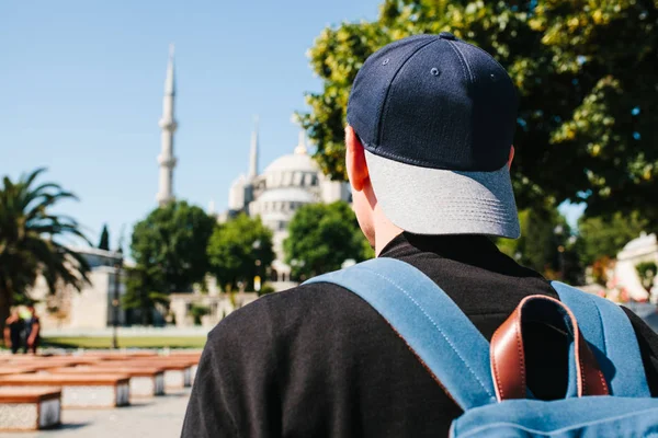 Un uomo con un berretto da baseball con uno zaino vicino alla moschea blu è uno spettacolo famoso a Istanbul. Viaggi, turismo, visite turistiche . — Foto Stock