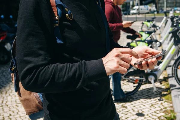 Un turista di sesso maschile noleggia una bicicletta o un mezzo di trasporto ambientale alternativo utilizzando un'applicazione mobile sul suo telefono. Oppure digita semplicemente un numero e chiama o usa Internet per strada . — Foto Stock