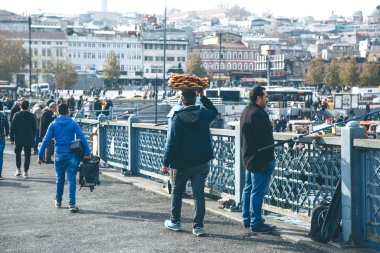 Türkiye, İstanbul, 29 Aralık 2019 - Satıcı Galata köprüsü boyunca yürüyor ve kafasında çok sayıda geleneksel Türk simidi taşıyor. Sokak yemekleri.