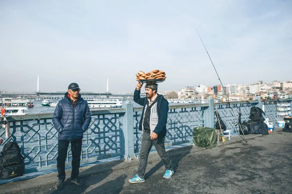 Turecko, Istanbul, 29. prosince 2019 - Prodávající kráčí po mostě Galata a nese na hlavě mnoho tradičních tureckých bagelů Simit. Obchod s potravinami — Stock fotografie