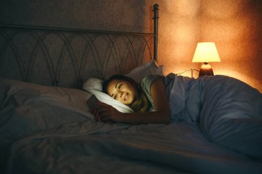 Girl with cell phone in bed.