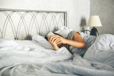Girl uses a cell phone in bed