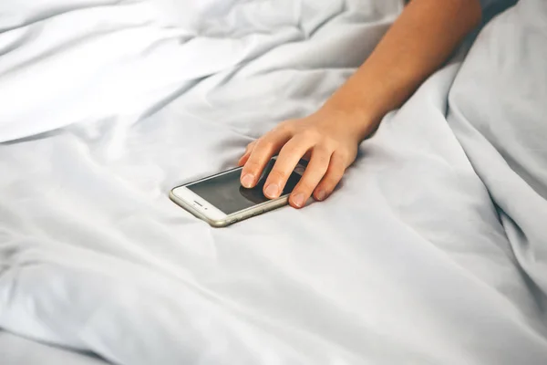 Close-up mano sostiene el teléfono en la cama — Foto de Stock