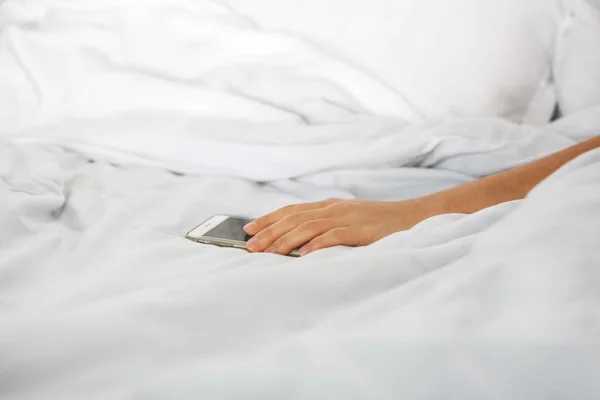 Close-up hand holds the phone in bed