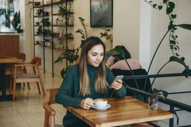 Kız bir cep telefonu kullanıyor ve kahve içiyor. Toplantısı var ya da sabah kapuçino içiyor ya da bembeyaz..