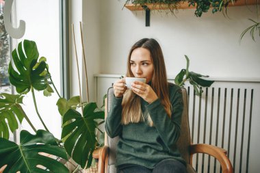 Bir kız kafede oturur ve sıcak bir içecek içer. Birini bekliyor ve bir toplantısı var ya da sabah içkisinin tadını çıkarıyor..
