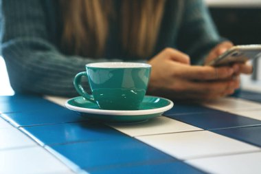 Bir kız kafede sıcak çay ya da kahve içer ve cep telefonu ya da cep telefonu kullanır..