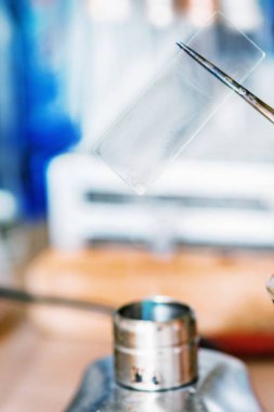 Laboratuvar iş mikroskop slayt alev üzerinde tutarak,