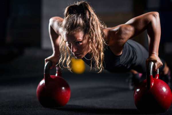 Woman athlete exercising with kettlebells indoors
