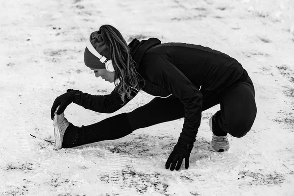 Female athlete exercising in park on winter day. Listening music and exercising