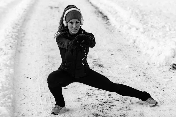 Female athlete exercising in park on winter day. Listening music and exercising