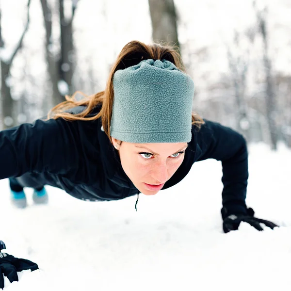 Female athlete exercising in park in winter with snow around the park. Listening music and exercising