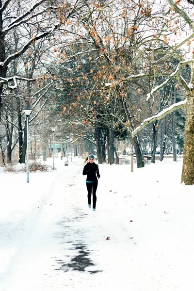 Female athlete jogging in park in winter with snow around the park. Listeninig music and exercising