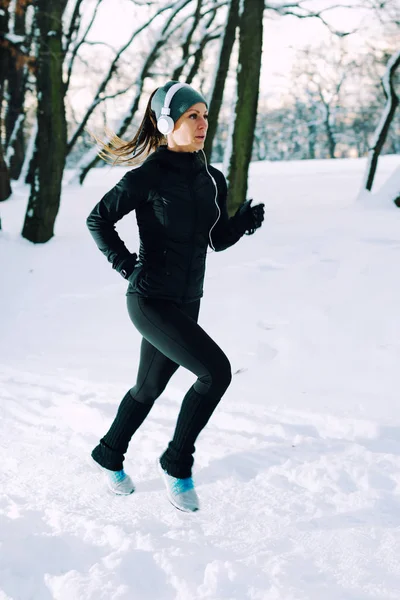 Female athlete jogging in park in winter with snow around the park. Listeninig music and exercising