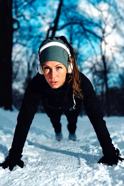 Female athlete exercising in park in winter with snow around the park. Listening music and exercising