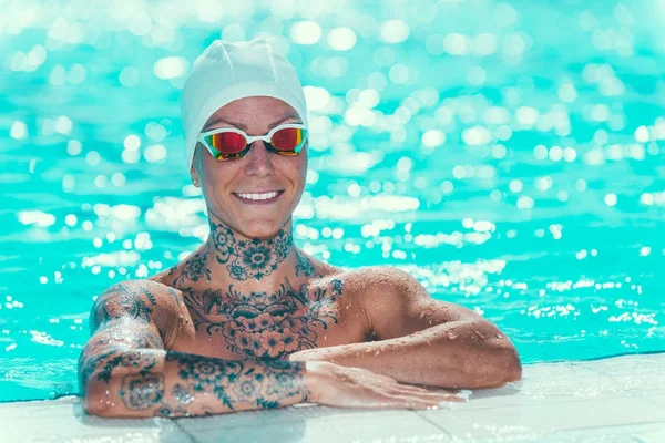 Portrait of female swimmer with tattoos on pool edge