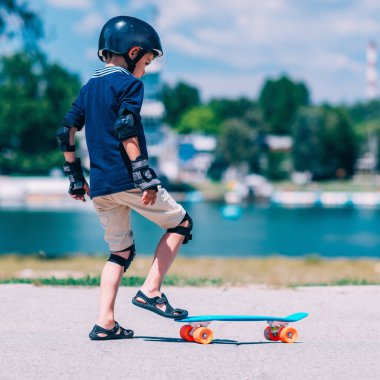 Küçük çocuk öğrenme skateborading göl kenarında park