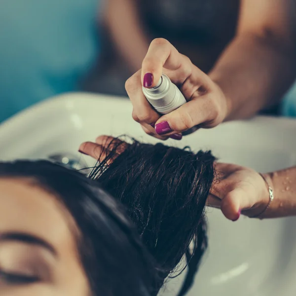 hairdresser spraying spray on woman hair in the salon