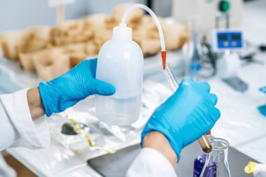 Toprak testi. Beyaz önlüklü kadın biyolog laboratuarda çözünmüş toprak örnekleriyle test tüpüne su döküyor. Toprağın Agrokimyasal incelemesi.