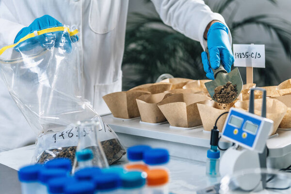 Soil Testing. Biologist's hand with protective gloves holding spatula with soil above samples separated in small containers.