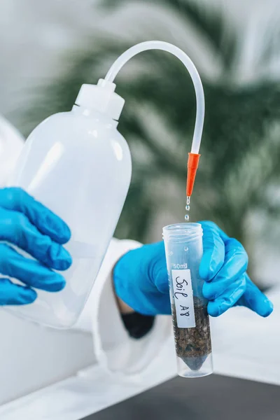 Soil Testing. Female biologist in white coat pouring water into test tube with dissolved samples of soil in laboratory. Agrochemical examination of soil.