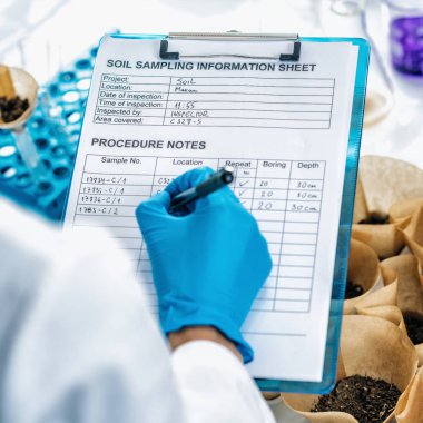 Toprak Örnekleri Test Laboratuvarı. Beyaz önlük giyen kadın bilim adamının laboratuarda notlar aldığı görüntüleri kapat.
