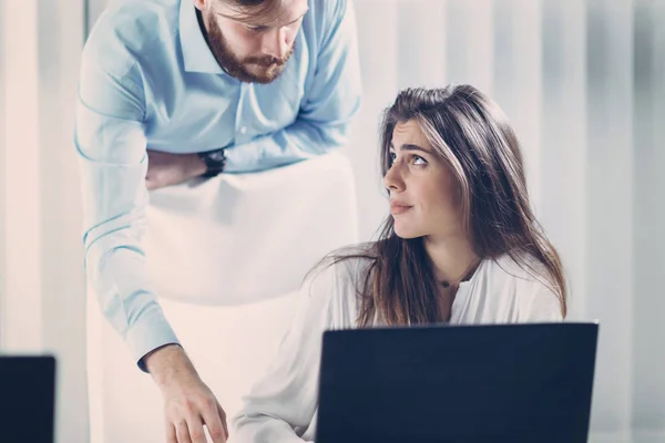 Working under pressure. Young ambitious male boss standing behind unhappy female worker and judging her work. Psychological harassment