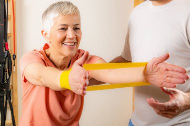 Spor salonunda lastik bantla egzersiz yapan son sınıf öğrencisi bir kadın. 