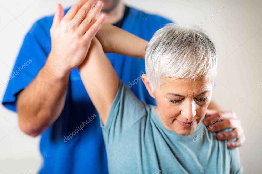 Therapist Checking Senior Womans Arm in Physical Therapy Office 