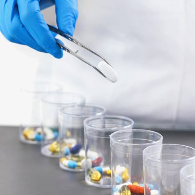 İlaçları sınıflandırıyorum. Doktorların elleri mavi eldivenlerle cımbız ilaçlarını gözlüklerle ayırıyor. Sağlık hizmetleri kavramı.