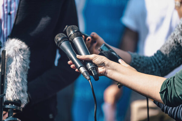 Female journalists interviewing male speaker, holding two microphones and dictaphone