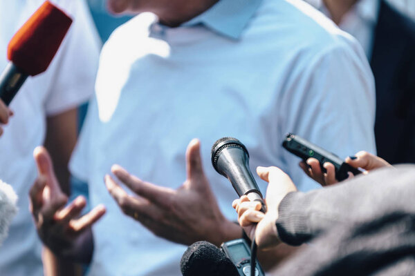 Journalists interviewing male speaker and holding microphones and mobile phone.