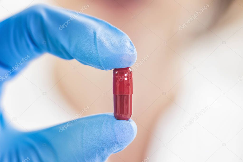 Female scientist holding red pill with blue gloves in laboratory. New Pill Research Concept