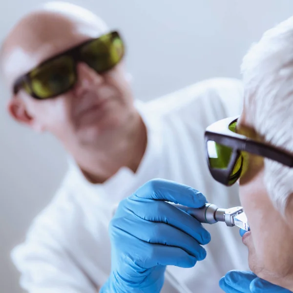 Laser Teeth Whitening. Dentist with safety goggles doing laser teeth whitening. Senior Dental Care.