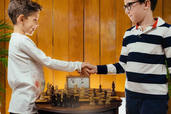 Little friends playing chess, having fun. Handshaking after game.