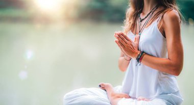 Genç kadın meditasyon yapıyor, doğada yoga yapıyor. Nilüfer çiçeğinde ellerin dua pozisyonunda oturuyor..