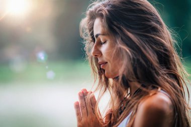 Genç kadın meditasyon yapıyor, doğada yoga yapıyor. Eller dua pozisyonunda..