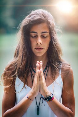 Genç kadın meditasyon yapıyor, doğada yoga yapıyor. Eller dua pozisyonunda..