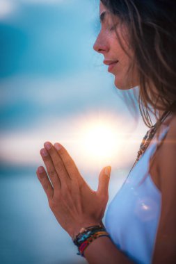Genç bir kadın gözleri kapalı meditasyon yapıyor. Elleri dua pozisyonunda yoga yapıyor..  