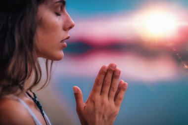 Genç bir kadın gözleri kapalı meditasyon yapıyor. Elleri dua pozisyonunda yoga yapıyor..  