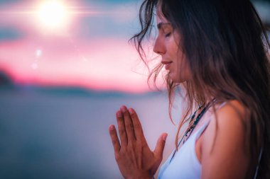 Genç bir kadın gözleri kapalı meditasyon yapıyor. Elleri dua pozisyonunda yoga yapıyor..  