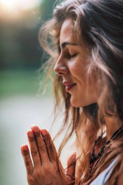 Genç kadın meditasyon yapıyor, doğada yoga yapıyor. Eller dua pozisyonunda..