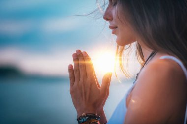 Genç bir kadın gözleri kapalı meditasyon yapıyor. Elleri dua pozisyonunda yoga yapıyor..  