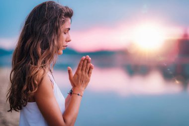 Genç bir kadın gözleri kapalı meditasyon yapıyor. Elleri dua pozisyonunda yoga yapıyor..  