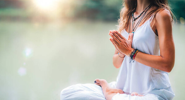 Young woman meditates, practicing yoga in nature. Sitting in lotus pose with hands in prayer position.