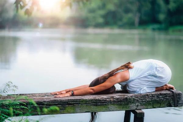 女はバラサナで瞑想湖のそばの子供のポーズ — ストック写真