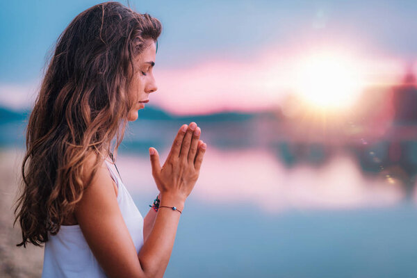 Young woman meditating with her eyes closed, practicing Yoga with hands in prayer position.  
