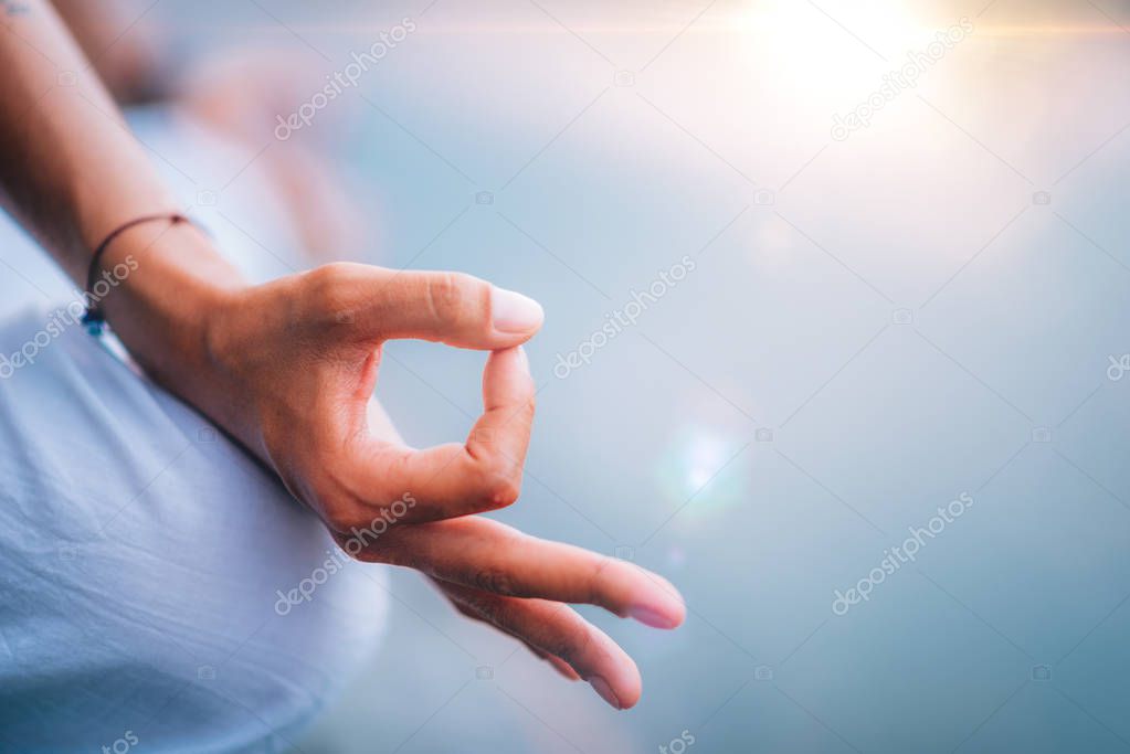 Close up image of womans hands in lotus position by the lake 